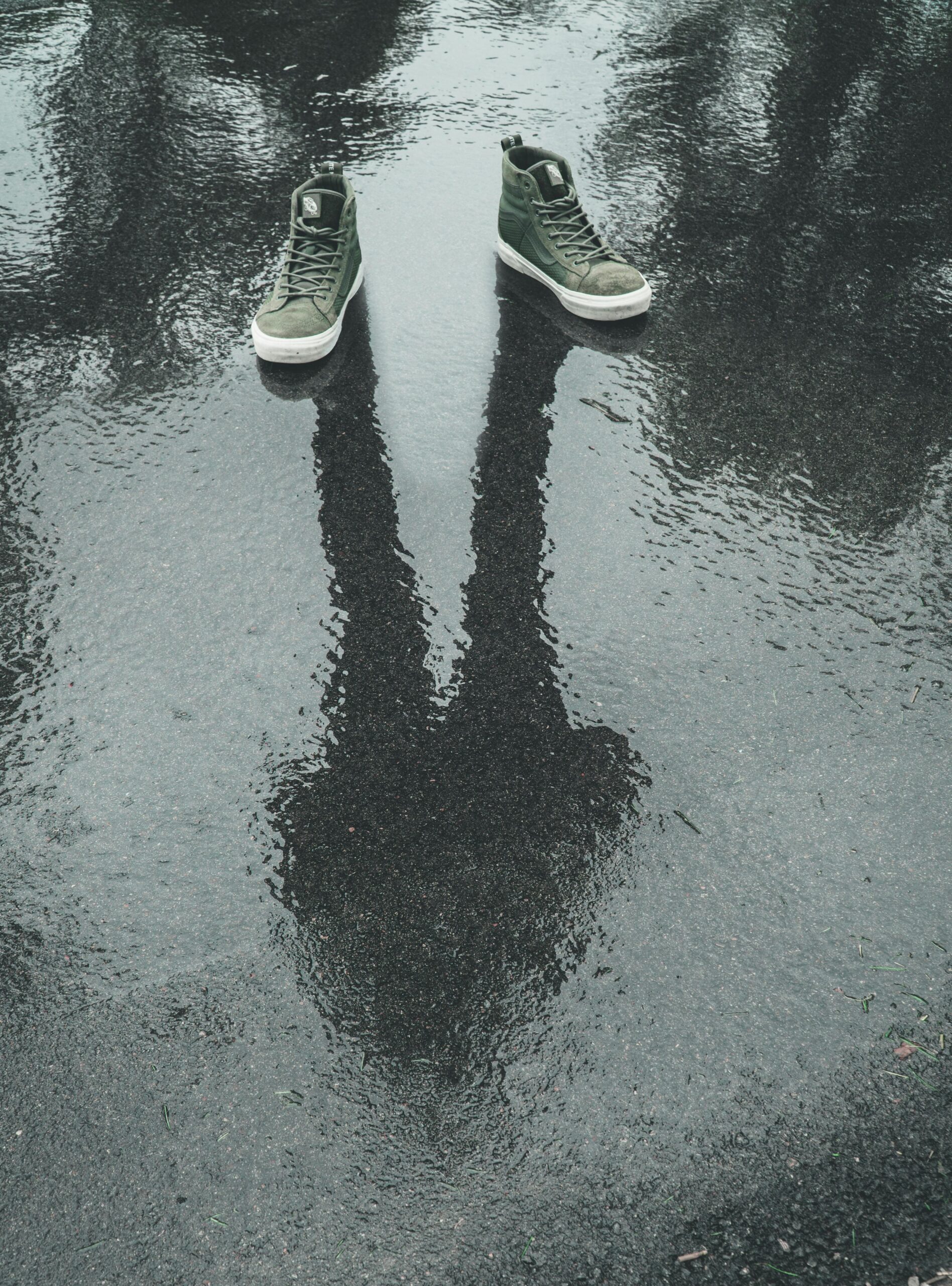Creative photo of sneakers with a human reflection on wet pavement, capturing mystery and creativity.